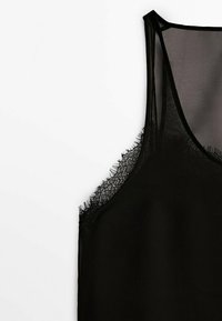 Camisola nera con tessuto trasparente e rifiniture in pizzo lungo il collo e l'orlo. Presenta spalline sottili e un design largo e fluido.