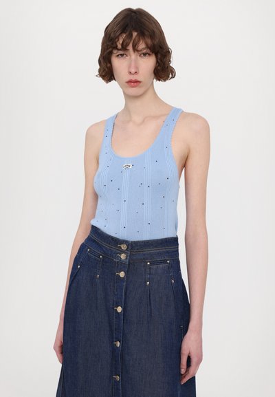 Lys blå ribbet tanktop med sorte prikker og en metallisk logo, kombinert med en mørk denimskjørt med gullknappeakenter og høy liv. 