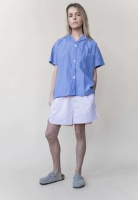 Blauw-wit gestreepte short-sleeve shirt met een klein zakje, gecombineerd met lichtroze shorts en grijze klompen. Eenvoudig, casual ontwerp.