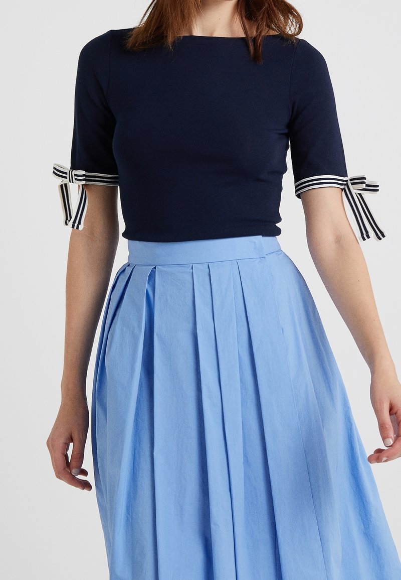 Haut marine à manches courtes avec des liens rayés, associé à une jupe plissée bleu clair. Texture lisse avec un design ajusté.