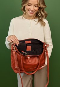 Bruine leren tote bag met zwarte binnenkant. Beschikt over twee handvatten, een afneembare schouderband en interieurzakken voor organisatie.