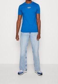 Modré bavlněné tričko s krátkými rukávy, na hrudi s logem Calvin Klein Jeans. Kombinováno se světle modrými džínami s rovnými nohavicemi a modrými teniskami.