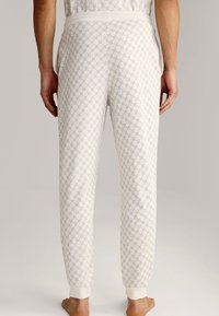 Pantalons de pyjama blancs avec un motif géométrique subtil, taille élastique, poches latérales et poignets élastiques aux chevilles. Tissu doux et texturé.