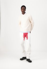 Un pull crème clair sur une chemise à col bleu, un pantalon blanc avec un bandana rouge et des bottines noires à chevilles. Lignes simples et épurées avec un contraste de couleurs audacieux.