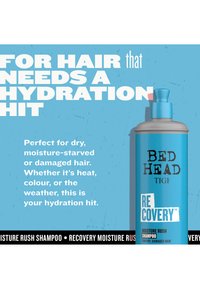 Blaue Flasche des Bed Head Recovery Moisture Rush Shampoos mit Text, der Feuchtigkeit für trockenes, geschädigtes Haar aufgrund von Hitze, Farbe oder Wetter bewirbt.