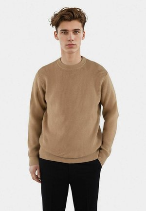 Beige ribbat tröja med rund hals och långa ärmar, tillverkad av textil med struktur, kombinerad med mörka byxor. En enkel och mångsidig design.