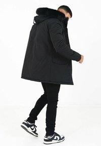 Svart parka med huva av fuskpäls, med dragkedja fram och sidofickor, bärs över svarta skinny jeans och svart-vita sneakers.