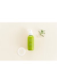 Grön sprayflaska med ett vitt pumplock märkt "Energizing Scalp Spray." Åtföljd av en genomskinlig skiva och en liten skål med gröna blad.