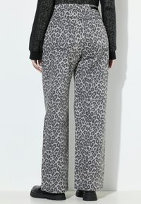 Pantaloni a gamba larga con stampa leopardata grigia, caratterizzati da una vita alta, due tasche posteriori e una linea dritta. Indossati con stivali neri alla caviglia.