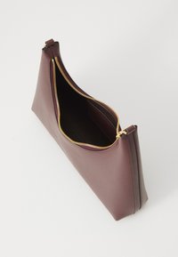 O poșetă clutch burgundă cu un fermoar aurit, parțial deschisă, dezvăluind un interior întunecat, asezată pe un fundal alb simplu.