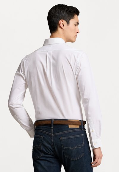 Witte langsl sleeve shirt met een standaard kraag, rugplooien, gecombineerd met donkere spijkerbroeken en een leren riem in het bruin. Eenvoudige knoopdetails.