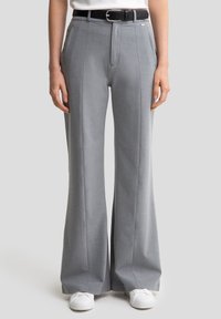 Un pantalon large gris clair en tissu texturé. Présente des plis marqués et une ceinture noire avec une boucle rectangulaire en argent.