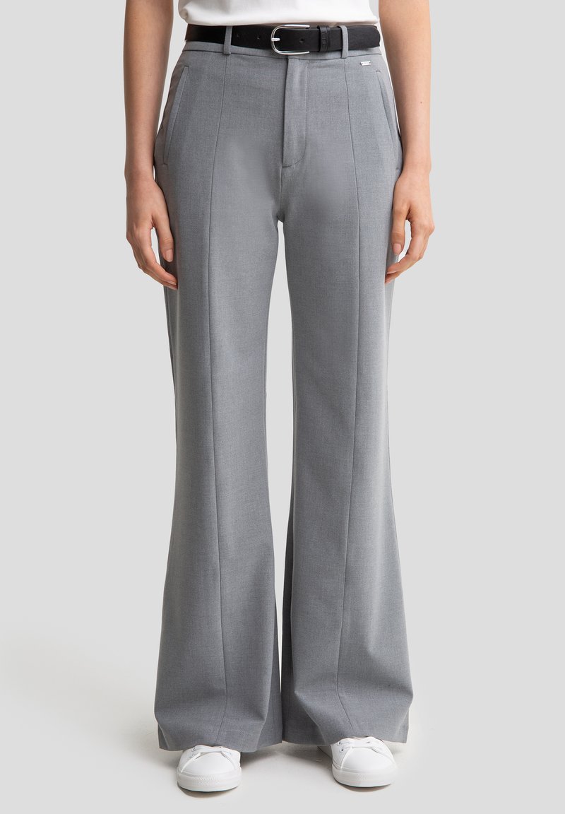 Un pantalon large gris clair en tissu texturé. Présente des plis marqués et une ceinture noire avec une boucle rectangulaire en argent.