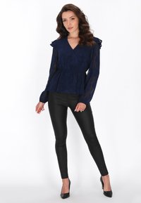 Mørkeblå, gennemsigtig bluse med flæser på skuldrene, indpakningsdesign, tekstureret blomster mønster; parret med tætsiddende sorte leggings og spidse hæle.