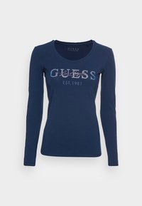 Granatowa koszulka z długim rękawem, wykonana z bawełny, z napisem "GUESS EST. 1981" w błyszczącym designie na przodzie. Okrągły dekolt.