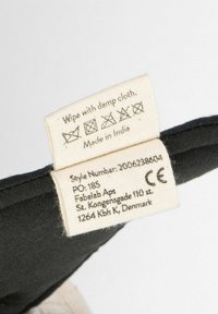 Črna tkanina nalepka z navodili za vzdrževanje, izdelana v Indiji. Vsebuje bele napise in ikone. Vključuje informacije o blagovni znamki in slogu.