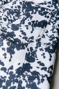 Λευκό ύφασμα με μαύρο και ναυτικό βελανιδιά σχεδιασμό· διαθέτει πίσω τσέπη με λεπτομέρειες ραφής. Το υλικό φαίνεται ανθεκτικό, σαν τζιν.