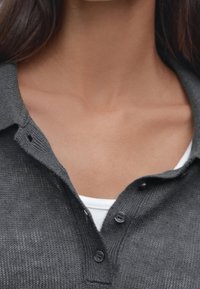 Camicia grigia con bottoni in tessuto strutturato, dotata di colletto e due bottoni all'collo, indossata sopra una camicia interna bianca.
