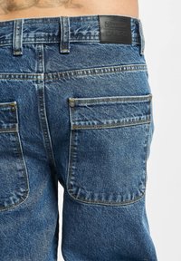 Denim-Jeans in einem mittleren Blauton, mit gestickten Gesäßtaschen, einem Logo-Patch am Bund und einem klassischen Fünf-Taschen-Design.
