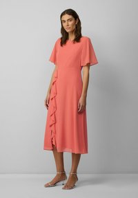 Koralli midi-mekko, jossa on lyhyet lepattelevat hihat, röyhelöyksityiskohtia sivuilla, sileä pinta ja ilmava malli. Yhdistetty hopeisiin sandaaleihin.