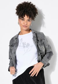 Šedá džínová bunda s vzorem a stříbrnými hroty; bílý tričko s květinovým designem z kamínků; černá manšestrová sukně.