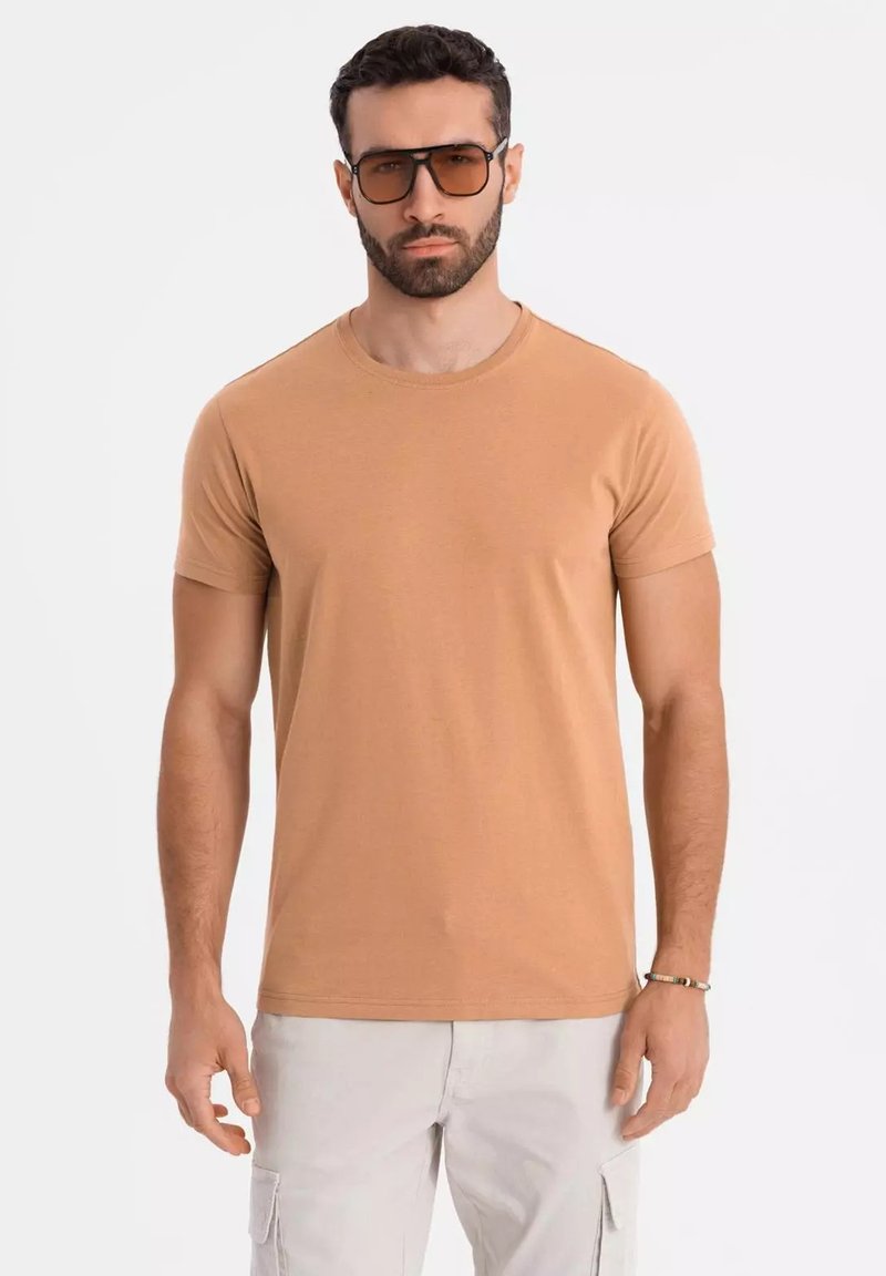 Tan kortærmet t-shirt i blødt bomuldsstof med rund halsudskæring. Båret med brune oversized solbriller og lyse bukser.
