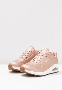 Rosa syntetiska träningsskor med ett perforerat mönster, vit mellansula och klar luftkudde; gummiyttersula med bra grepp.