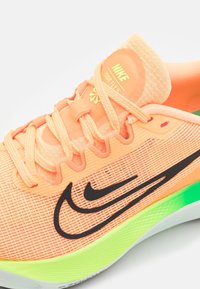 Baskets Nike Zoom Fly 5 orange vif avec logo double swoosh noir, lacets pêche et détails de semelle vert néon sur fond blanc.