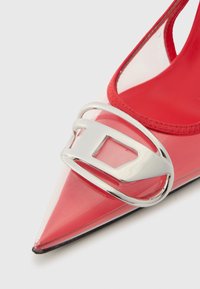 Κόκκινο παπούτσι στιλέτο από λουστρίνι με μυτερή μύτη, διαφανείς πλευρές και έντονο ασημένιο πόμολο στο εμπρός μέρος. Μαύρη σόλα.