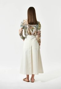 Gonna bianca fino al ginocchio con uno spacco posteriore e due tasche sul retro. Abbinata a una blusa a fiori multicolore.