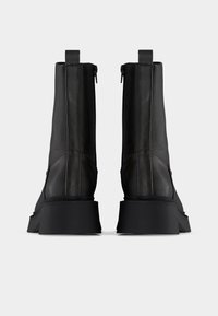 Ζευγάρι μαύρων δερμάτινων μποτάκια αστραγάλου με χοντρές σόλες πλατφόρμας, πίσω λουράκια για έλξη και φερμουάρ, σε απλό ανοιχτό φόντο.