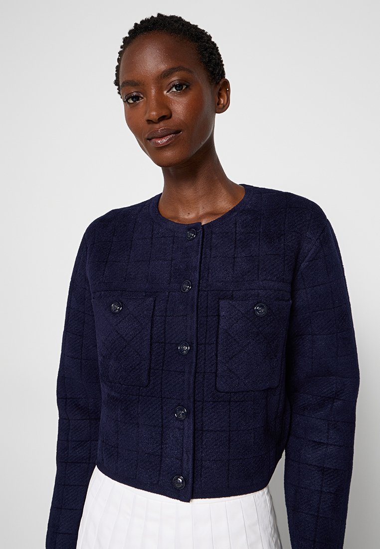 Granatowa, krótka kurtka z pikowanej tkaniny, z czterema kieszeniami i okrągłym dekoltem, zapinana na sześć pasujących guzików.