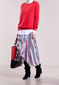 Jersey de punto rojo sobre una camisa blanca, acompañado de una falda a rayas multicolor y botas negras hasta la rodilla. Incluye un bolso negro y rojo.