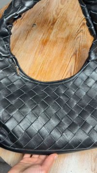 Mustast punutud nahast käekott, millel on suur, ümar kuju ja reguleeritav rihm. Omadusteks on tõmblukuga sulgumine ja tekstureeritud pind.