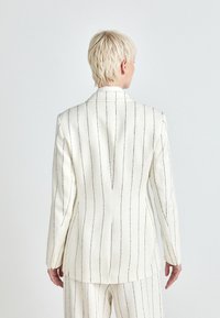 Wit gestreepte blazer met zwarte verticale lijnen, voorzien van een gelapte kraag en een getailleerde pasvorm. De achterkant heeft een middelste vent en gestructureerde schouders.