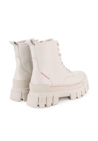 Botas de tobillo de cuero blanco con una suela de goma gruesa y texturizada. Las características incluyen cordones, tiradores y un detalle de costura en color naranja.
