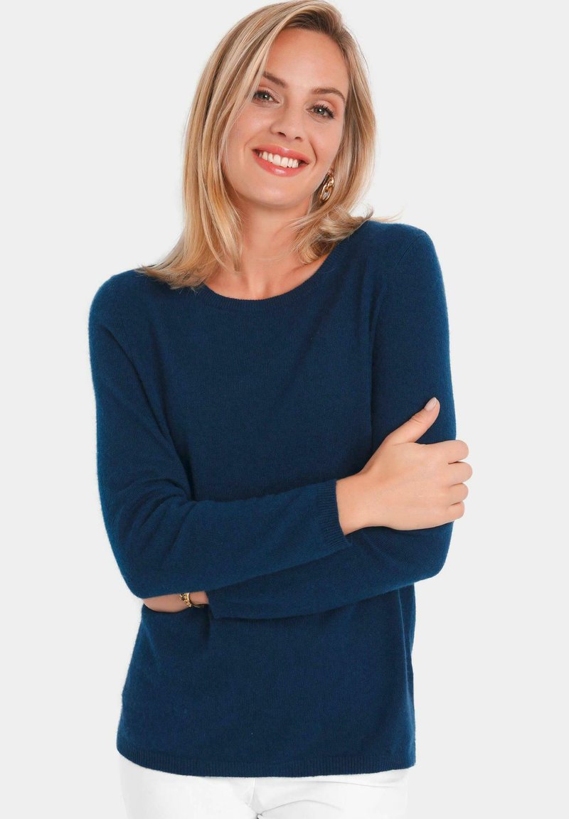 Navyblauwe gebreide trui met lange mouwen en een ronde hals, met een zachte textuur. Het model poseert met gekruiste armen tegen een witte achtergrond.