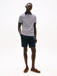 Stripet polo skjorte i blått og hvitt, marineblå krage, kombinert med marineblå shorts og brune båtsko. Glatte teksturer og tettsittende design.