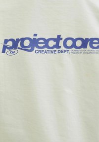 Lys grøn bomulds t-shirt med fed blå tekst, der siger "project core CREATIVE DEPT." Inkluderer varemærkesymbol; glat tekstur.