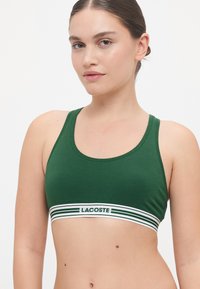 Πράσινο αθλητικό σουτιέν από βαμβάκι με εφαρμοστή σχεδίαση και φαρδιά ελαστική ζώνη με ρίγες που φέρει το κείμενο "LACOSTE" σε λευκό και πράσινο. Λείο υλικό.