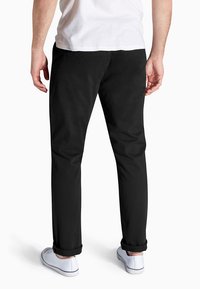 Schwarze Baumwollhosen mit geradem Schnitt, ausgerollten Bündchen und glatter Textur. Getragen mit weißen Freizeitschuhen.