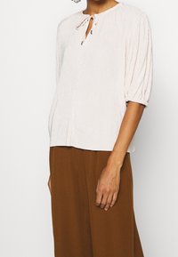 Světle růžová texturovaná blůza s kulatým výstřihem a zavazováním uprostřed. Obsahuje vypinflé krátké rukávy a volný střih.