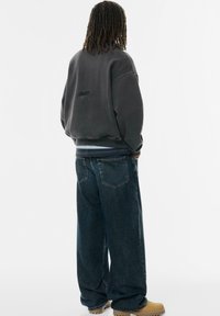Czarnoszary oversize'owy sweter z prążkowanymi mankietami, zestawiony z luźnymi, ciemnoniebieskimi dżinsami. Kremowe botki dopełniają stylizację.