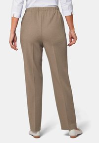 Tan geribbelde broeken met een elastische tailleband, rechte pijpen en een gladde textuur, gecombineerd met lichtgekleurde schoenen.