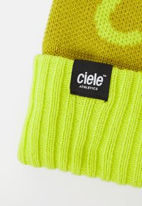 Knitted beanie in a yellow and neon green color scheme, featuring a ribbed texture and a black label with "ciele ATHLETICS" branding.
