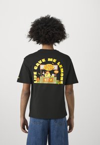 Camiseta negra con un gráfico colorido de un puesto de limones en la parte posterior y el texto: "¡LA VIDA ME DIO LIMONES!" con ilustraciones de frutas. Mangas cortas.