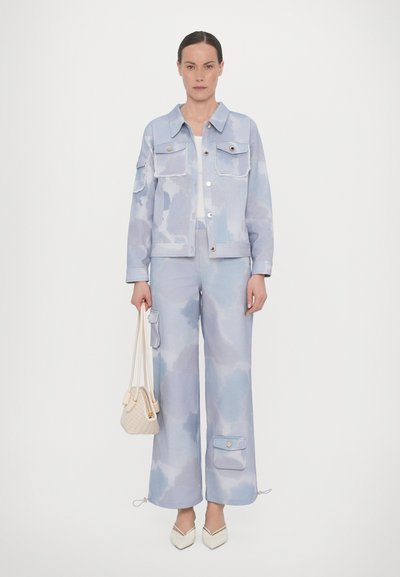 Lyseblå denimjakke og bukser med sky-lignende mønstre, med to forlommer og snørekanter, parret med en vævet taske.