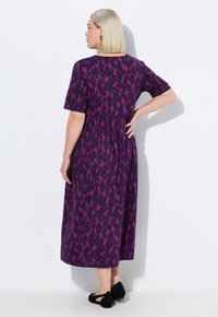 Abito viola con stampa leopardata rosa, di lunghezza media, maniche corte e dettaglio in vita arricciato. La modella indossa scarpe nere.