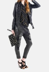 Svart läderjacka med nitar, mönstrad topp, slitna svarta jeans och svarta strap high heel sandaler. Clutchväska med ögon.