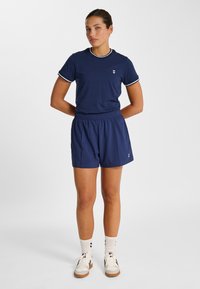 Mörkblå atletisk tröja med vita detaljer och logotyp, kombinerad med matchande shorts. Båda har en slät textur och ett elastiskt midjeband.